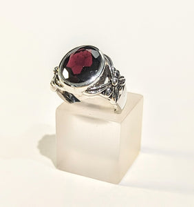 Large oval faceted garnet ring set in sterling silver with flower motif on the sides.
